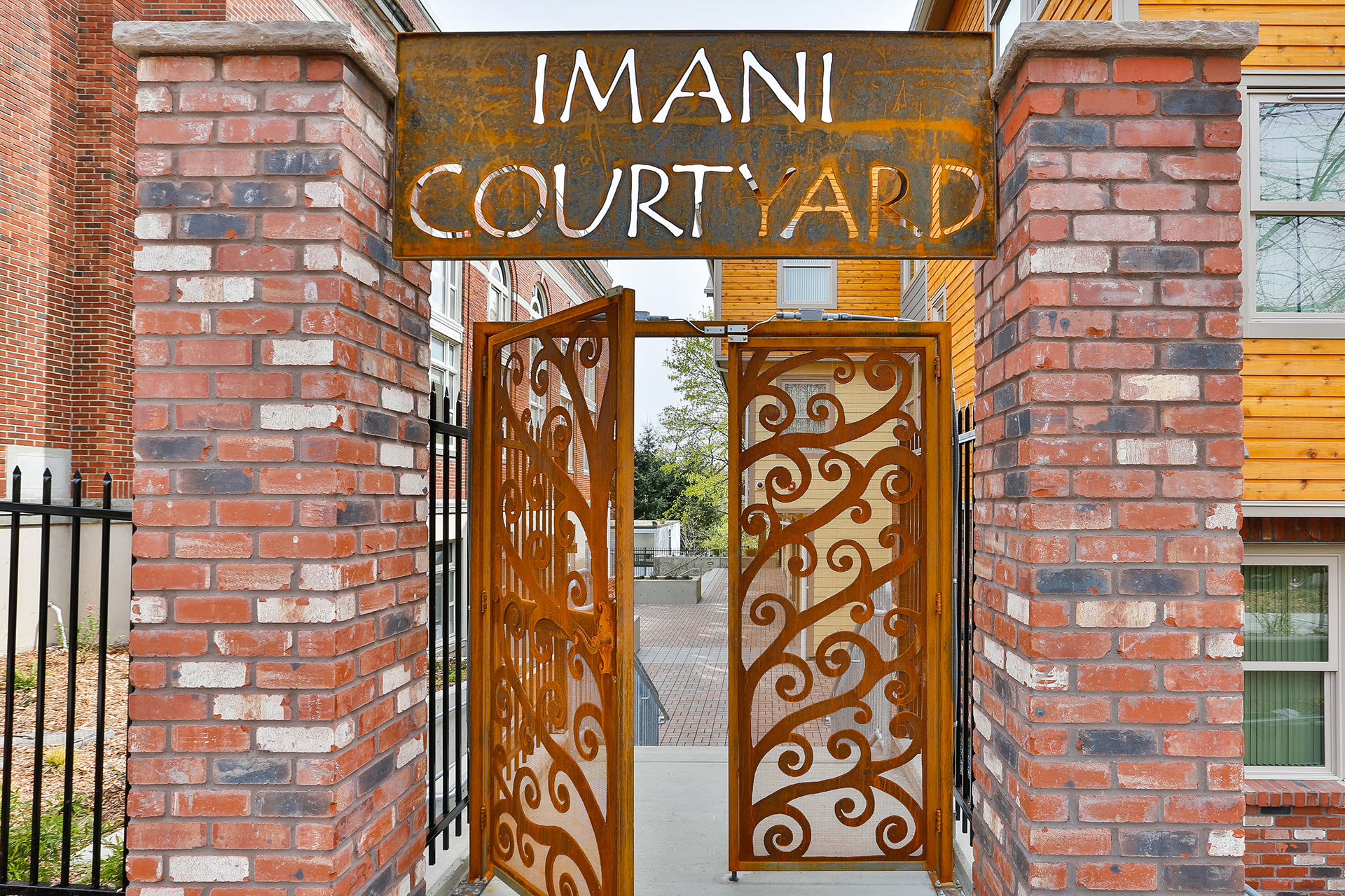The entry to Imani Courtyard has an artistic copper gate nestled between two red brick pillars.