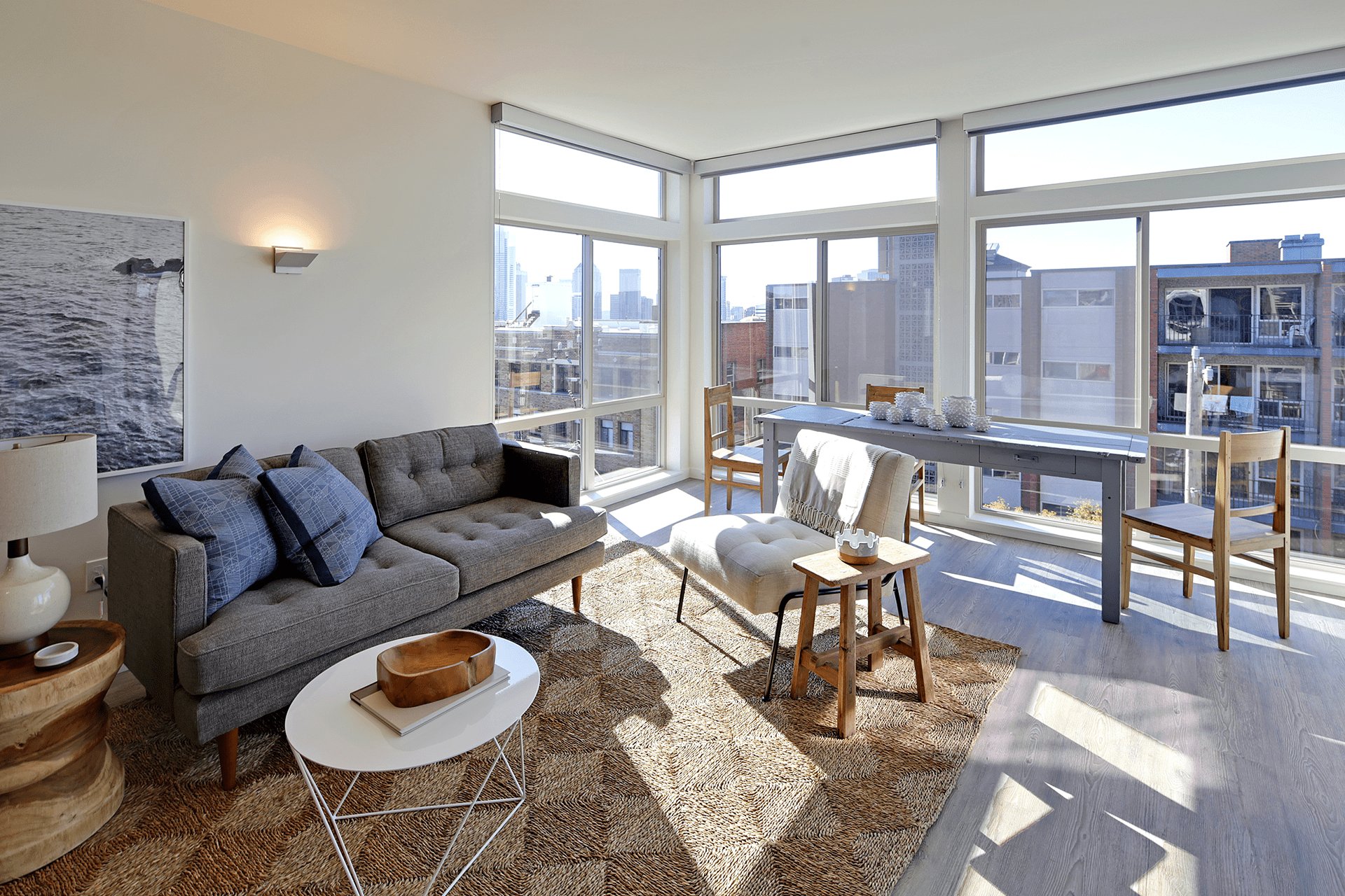 The interior of one of the units in the Lexicon Apartment building includes gray wood floors, a seating area, dining table, and large corner windows.
