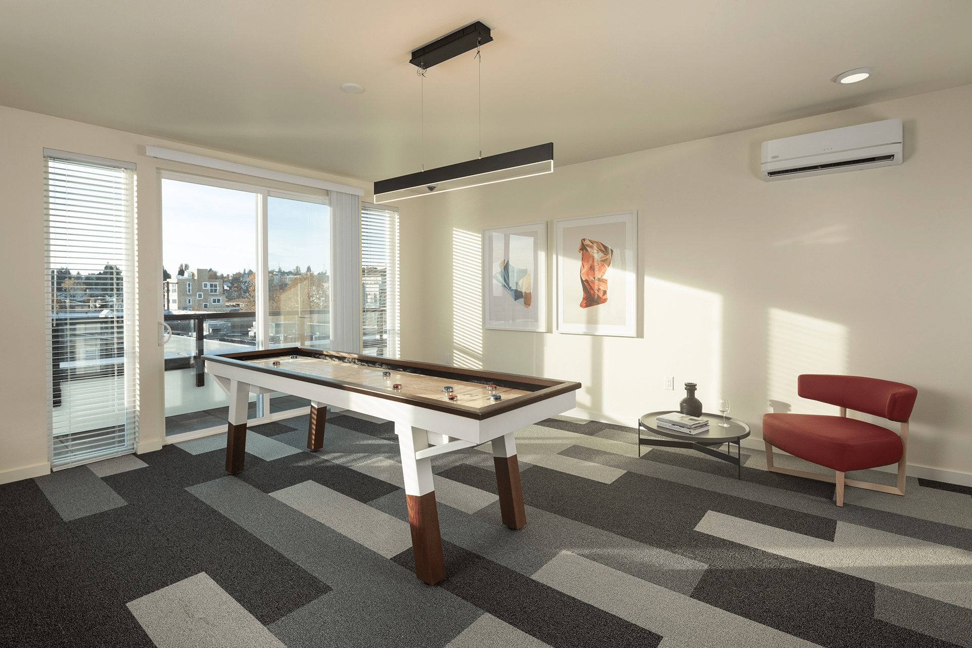 An interior community space at the Roosevelt Apartments features a geographic gray floor, tall windows, and a shuffleboard table.
