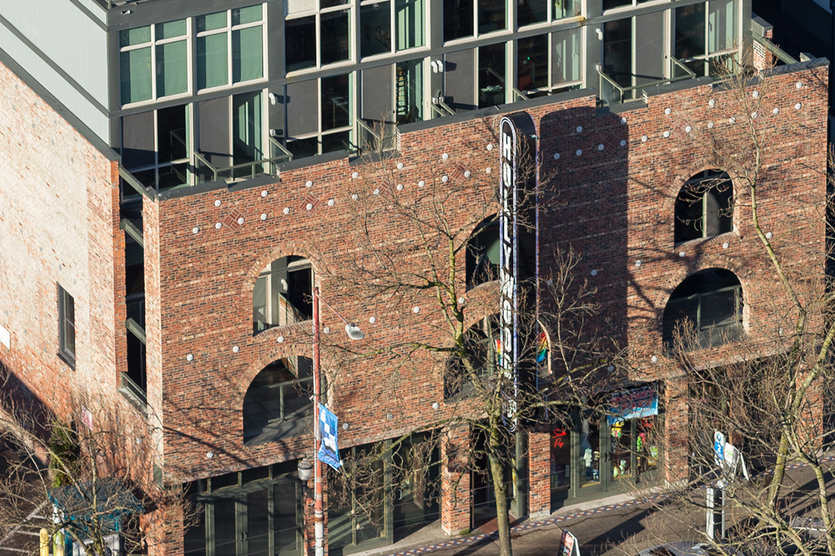 A distant shot of the Hollywood Lofts building. Its upper floors are painted gray and have tall square windows, while the rest of the building is red brick. The front of the building features rounded windows.
