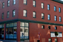 A corner picture of the New Central Hotel, a red brick building with tall corner windows and rows of evenly spaced smaller windows along the upper floors.