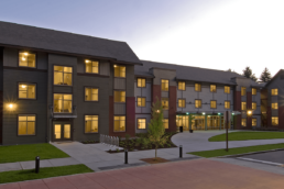 Parsons Hall, a long dark brown building with three floors, a large lawn, and a curved sidewalk in the front courtyard,