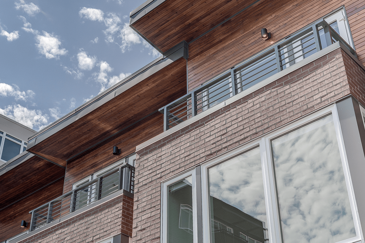 A very close shot of the University Apartments building shows its architectural detail with tan wood slats, red brick, tall windows, and gray metal railing on the balconies.